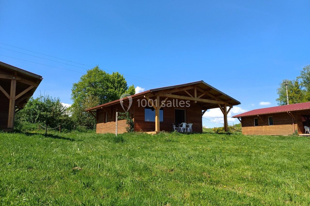 Chalet en bois avec terrasse, situé sur une pelouse verdoyante sous un ciel bleu dégagé.