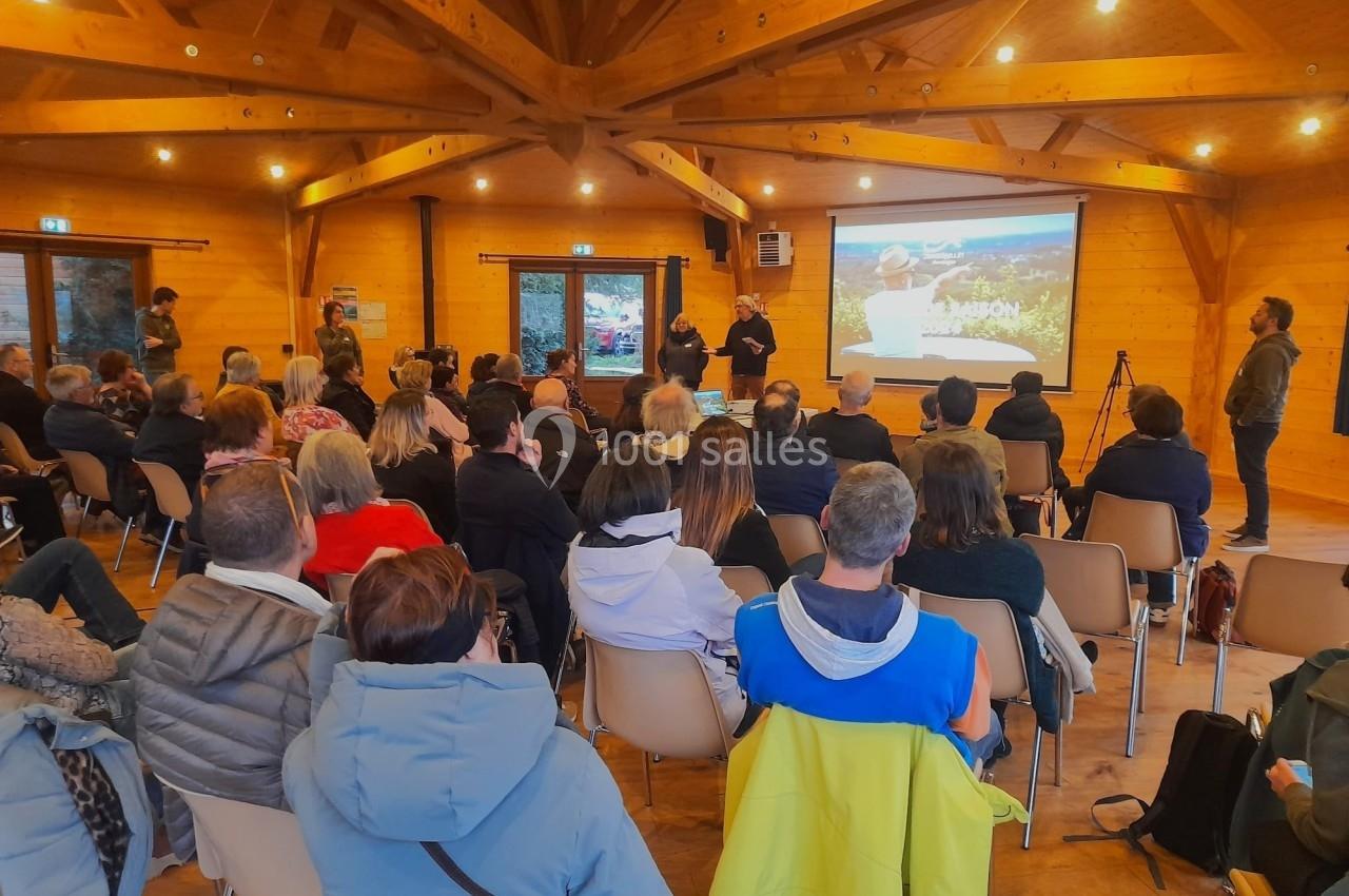 Un groupe de personnes assises dans une salle en bois assistent à une présentation projetée sur un écran.