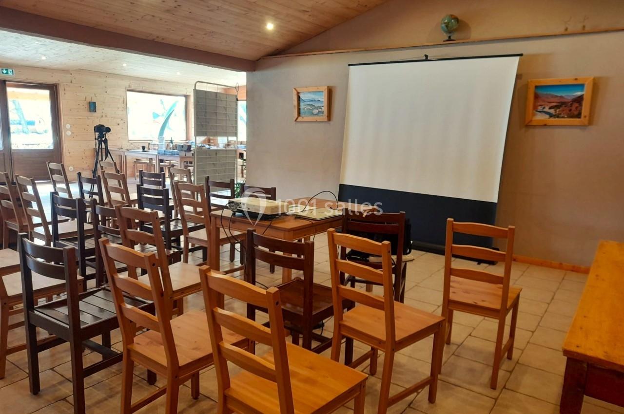 Salle avec des chaises en bois disposées face à un écran de projection dans un espace lumineux au plafond en bois.