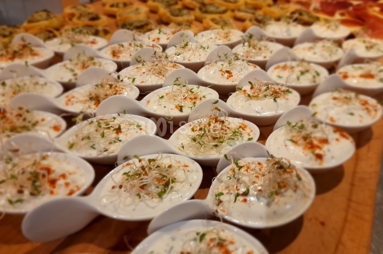Petites cuillères en porcelaine garnies de crème blanche, herbes fraîches et paprika, disposées sur une table en bois.