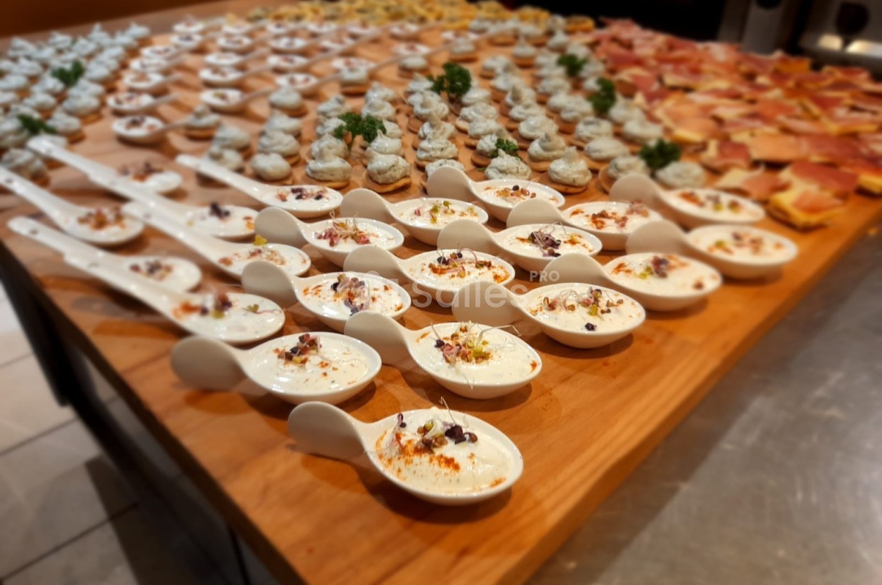Plateau en bois garni de cuillères apéritives et de bouchées variées, disposées pour un buffet.