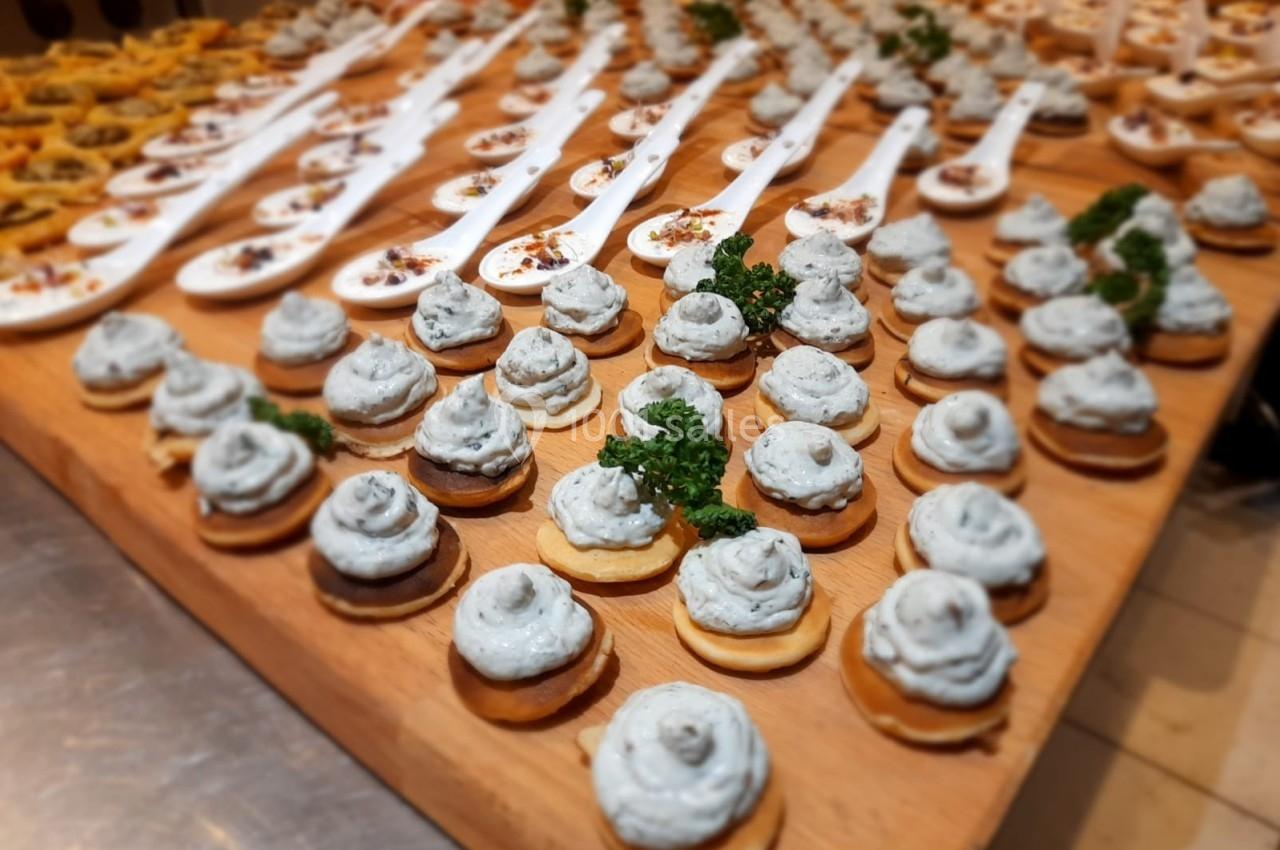 Plateau de bouchées apéritives variées, incluant des cuillères et des toasts garnis de mousse et d'herbes fraîches.