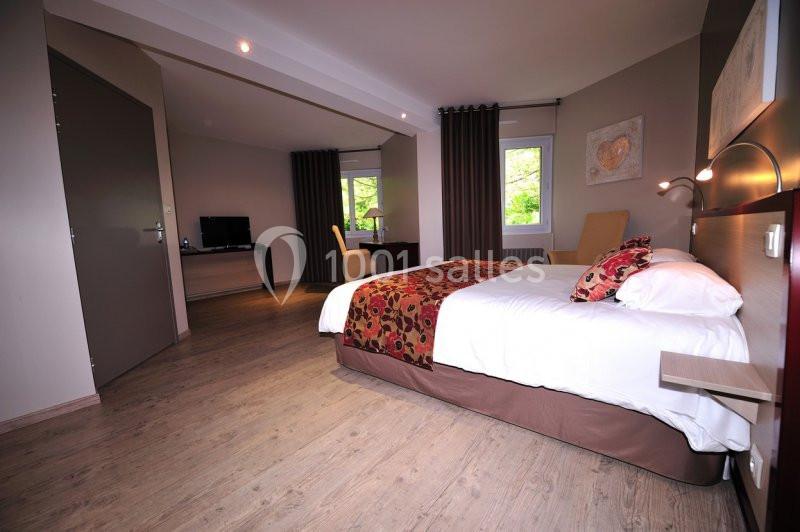 Chambre spacieuse avec lit double, bureau, télévision et grandes fenêtres donnant sur un extérieur verdoyant.