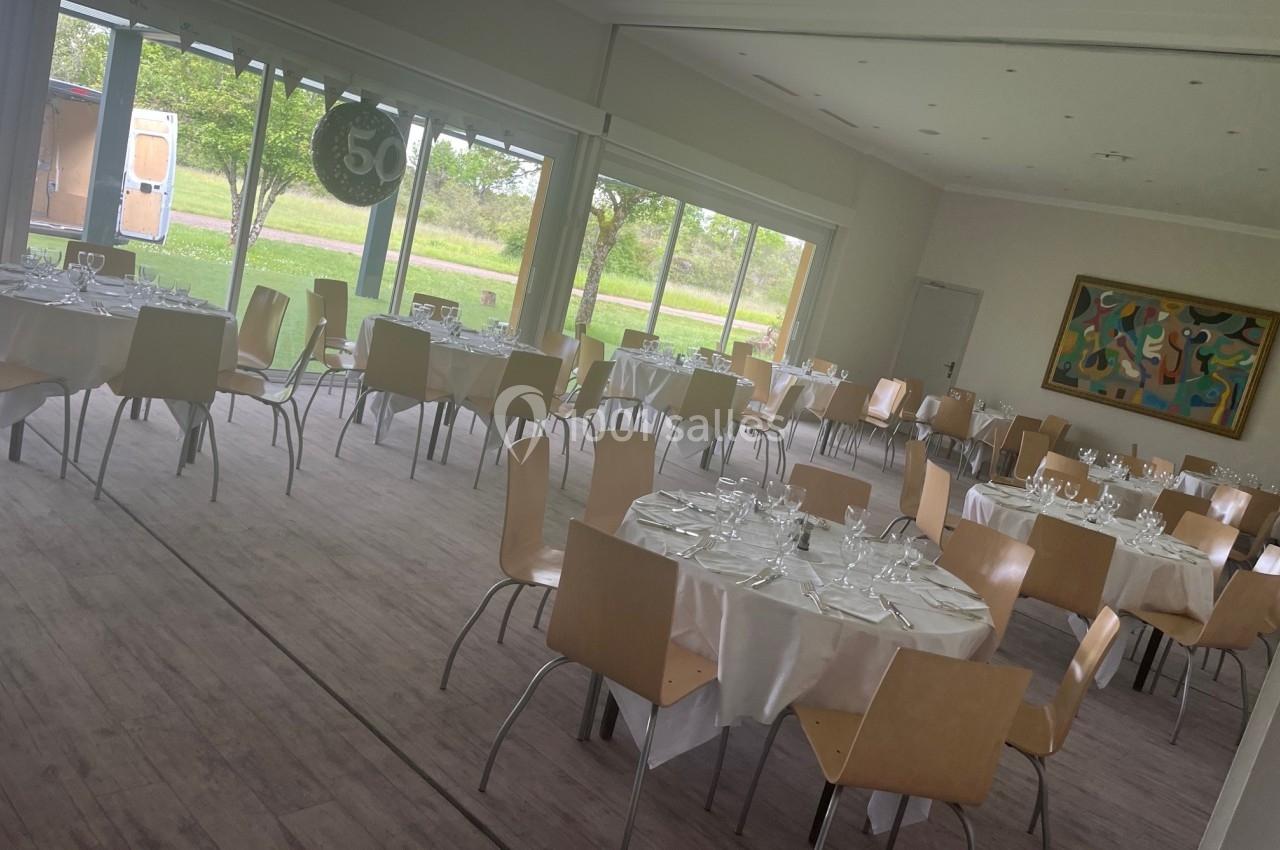 Salle de réception lumineuse avec des tables rondes dressées, chaises en bois clair et vue sur un espace extérieur verdoyant.