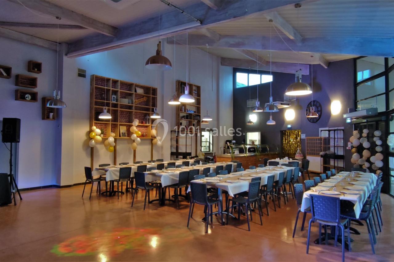 Salle de réception décorée avec des tables dressées, des ballons dorés et un éclairage tamisé.