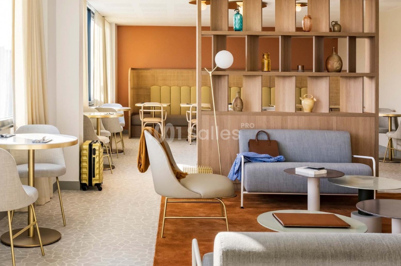 Espace salon lumineux avec mobilier moderne, cloison en bois, tables, chaises et valise jaune près d'une fenêtre.
