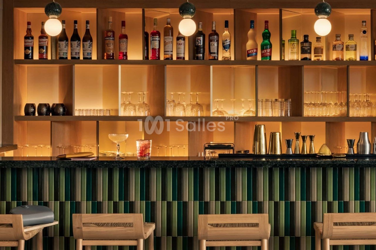 Bar avec comptoir en bois, étagères éclairées contenant bouteilles, verres et accessoires de mixologie.