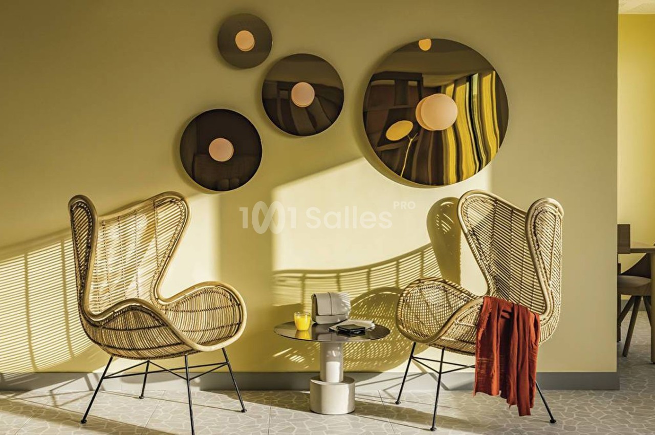Deux fauteuils en rotin face à une table basse, devant un mur jaune décoré de miroirs ronds.