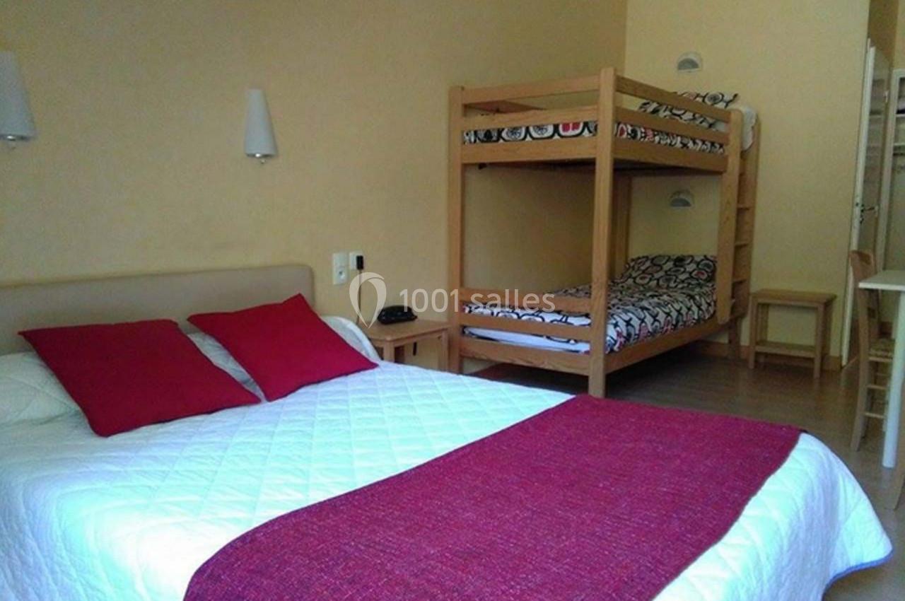 Chambre avec un lit double, des lits superposés en bois, murs clairs et mobilier simple.