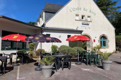 Miniature Location salle Ergué-Gabéric (Finistère) - L’Orée du Bois #1 Vue sur un jardin avec des arbres, une maison blanche et un paysage de campagne sous un ciel nuageux.