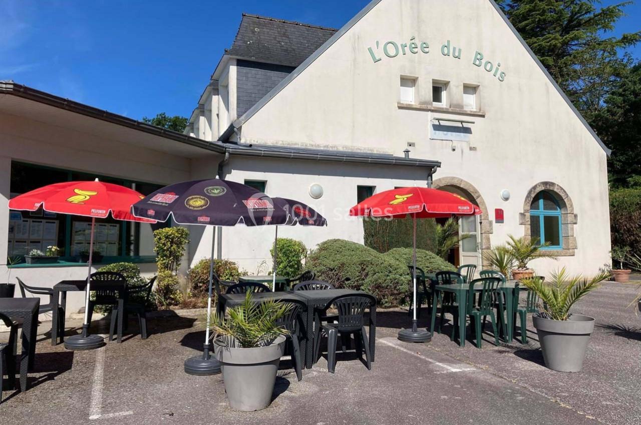 Terrasse extérieure d'un restaurant avec tables, chaises, parasols colorés et façade blanche en arrière-plan.