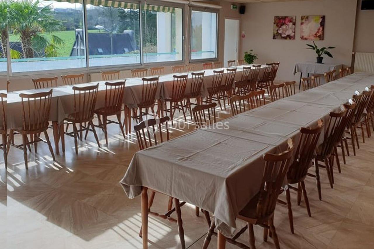 Salle lumineuse avec de longues tables rectangulaires recouvertes de nappes blanches et des chaises en bois.