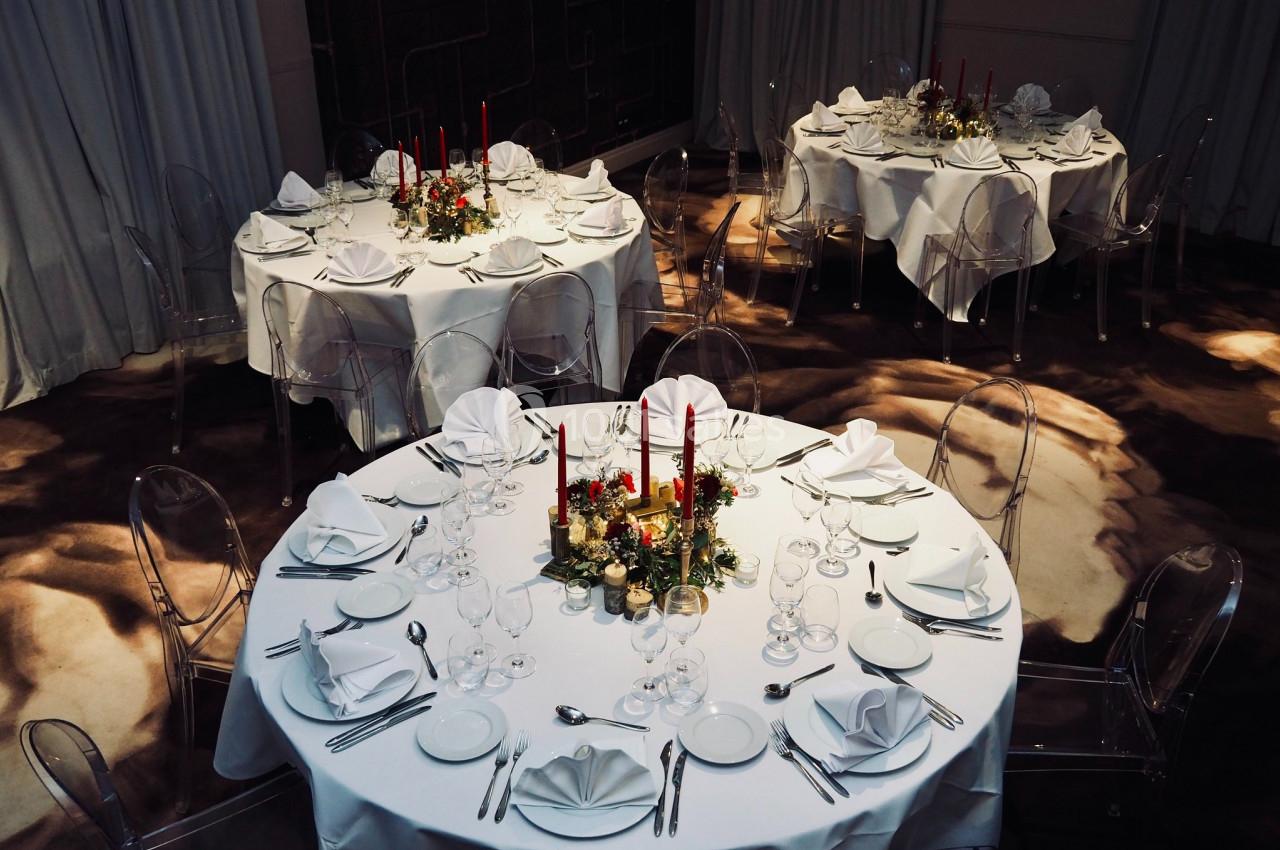 Location salle Lille (Nord) - Les Salons de l'Urban #19 Tables rondes élégamment dressées avec nappes blanches, chandeliers rouges et décorations florales dans une salle feutrée.