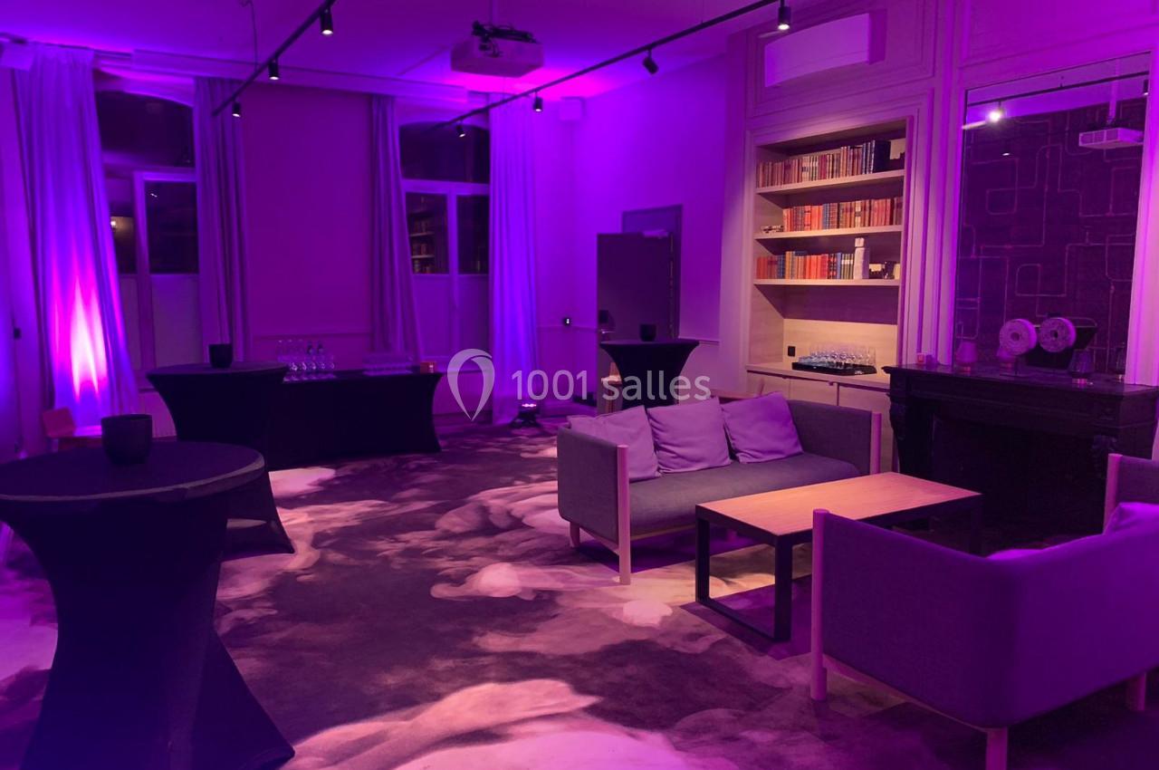 Location salle Lille (Nord) - Les Salons de l'Urban #20 Salle de réception éclairée de lumières violettes, avec canapés, tables basses, bibliothèques et nappes noires.