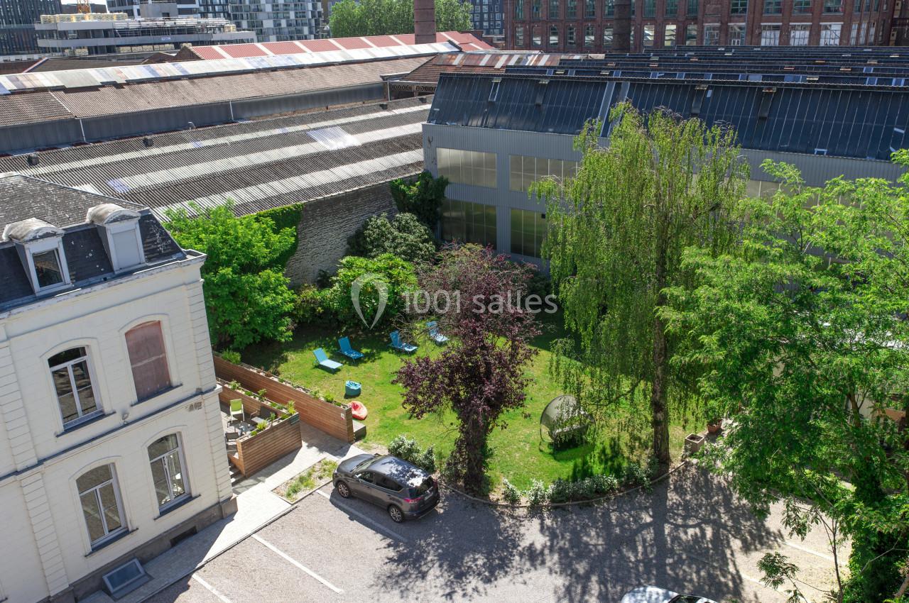 Location salle Lille (Nord) - Les Salons de l'Urban #10 Vue aérienne d'une cour arborée avec pelouse, chaises longues, arbres et bâtiments industriels en arrière-plan.