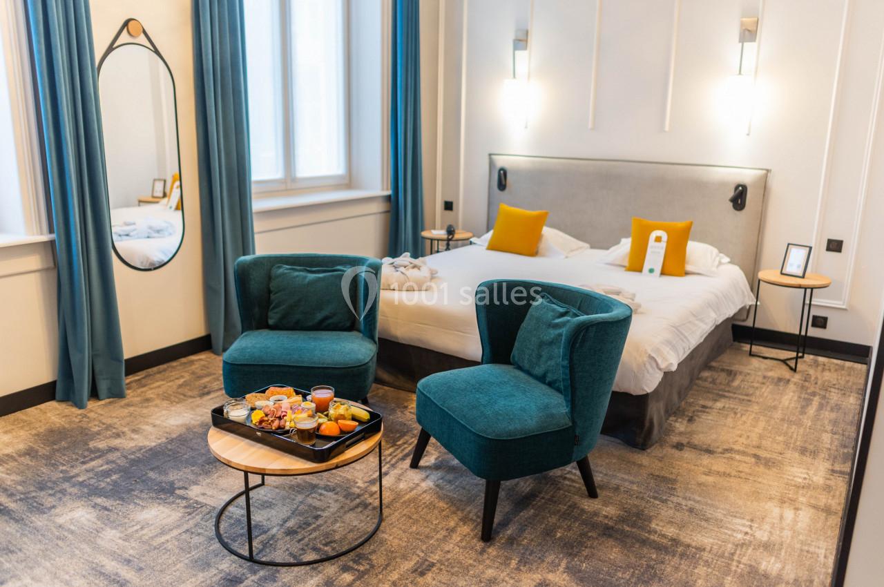 Location salle Lille (Nord) - Les Salons de l'Urban #35 Chambre lumineuse avec lit double, fauteuils verts, table basse et plateau de petit-déjeuner, décor moderne et épuré.