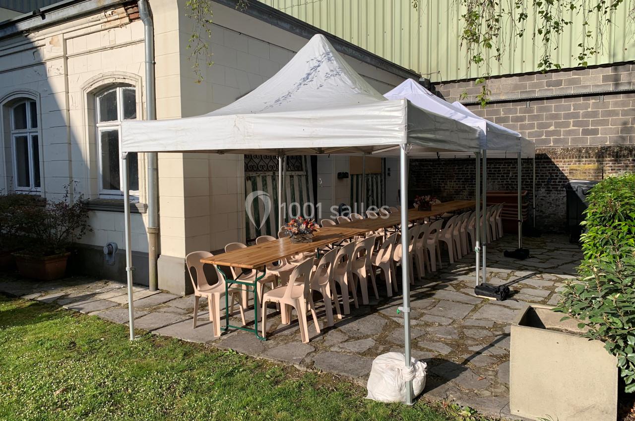 Location salle Lille (Nord) - Les Salons de l'Urban #29 Deux tentes blanches abritent une longue table avec des chaises en plastique beige, installées dans une cour pavée.