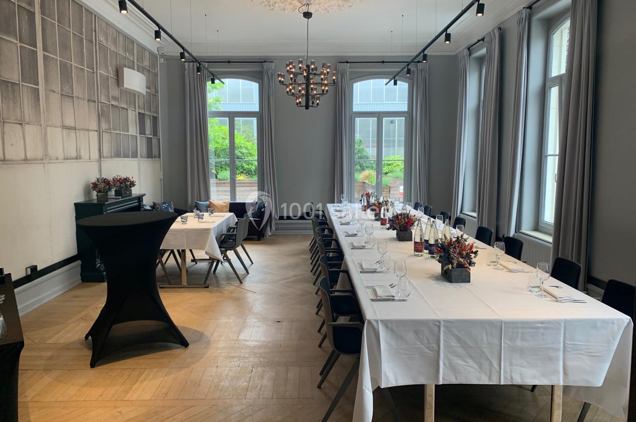 Location salle Lille (Nord) - Les Salons de l'Urban #7 Salle lumineuse avec de grandes fenêtres, tables dressées avec nappes blanches, chaises noires et décorations florales.