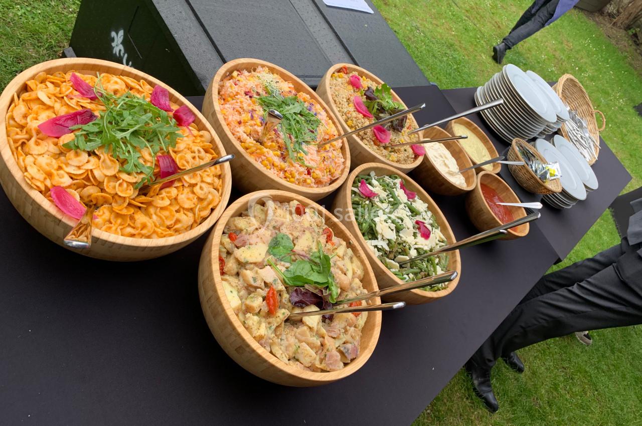 Location salle Lille (Nord) - Les Salons de l'Urban #15 Buffet en plein air avec des salades variées présentées dans des bols en bois, accompagné d'assiettes et de couverts.