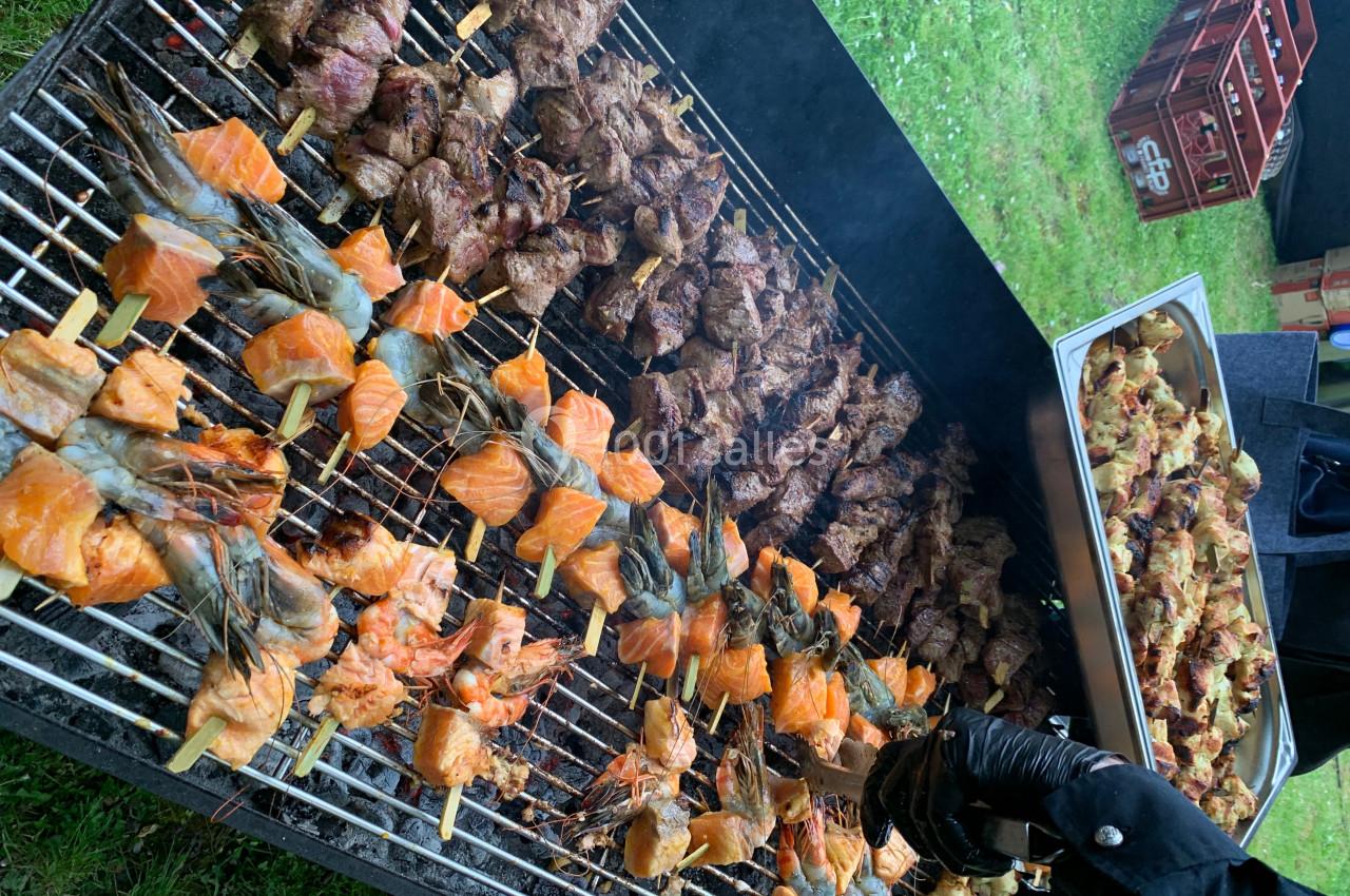 Location salle Lille (Nord) - Les Salons de l'Urban #28 Brochettes de crevettes, saumon et viande grillant sur un barbecue en plein air, avec un plateau de viande à côté.