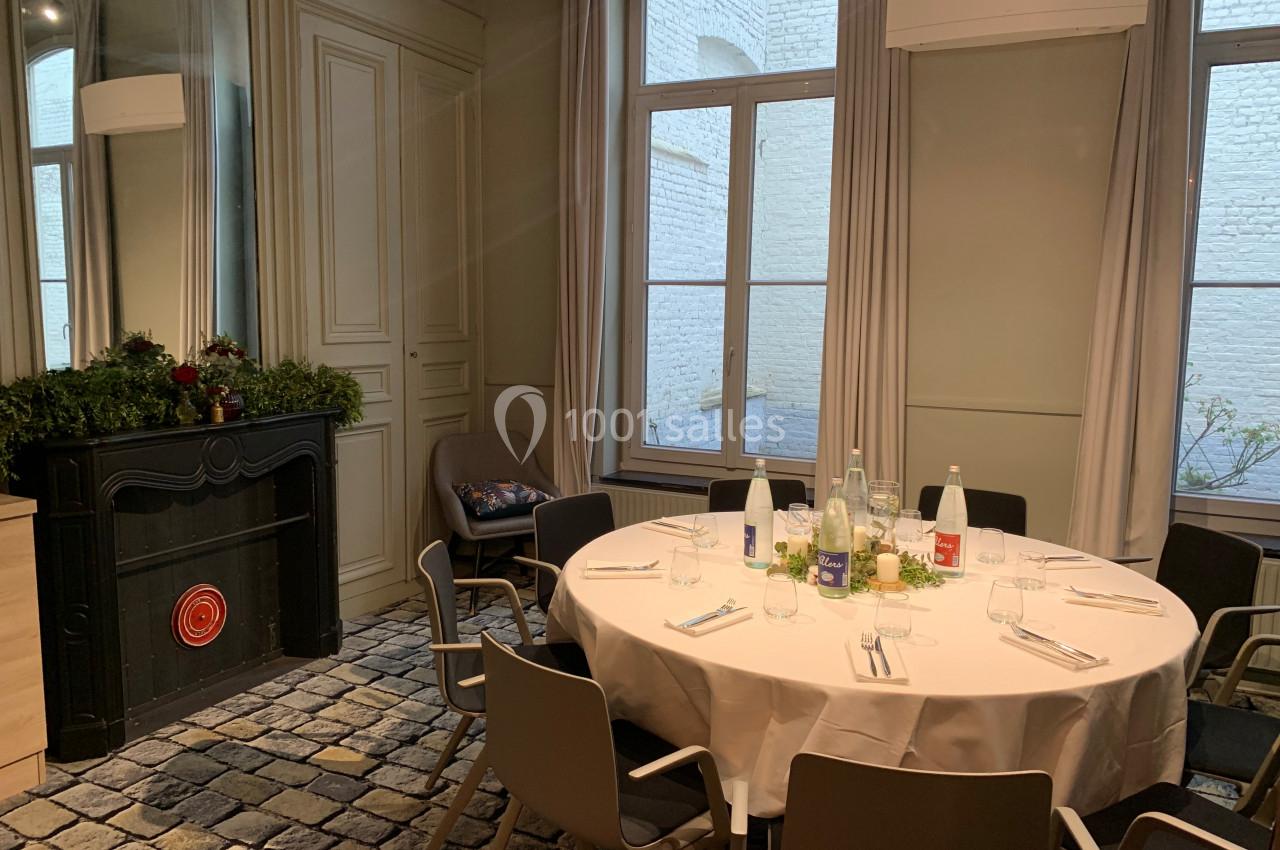 Location salle Lille (Nord) - Les Salons de l'Urban #33 Salle lumineuse avec table ronde dressée, chaises modernes, cheminée décorée et grandes fenêtres donnant sur une cour.