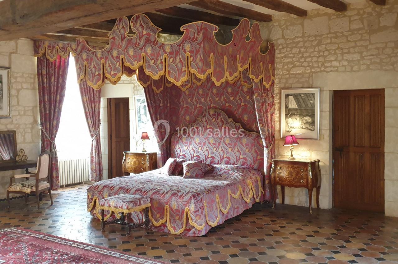Chambre avec lit à baldaquin, rideaux décoratifs, meubles anciens et murs en pierre apparente.