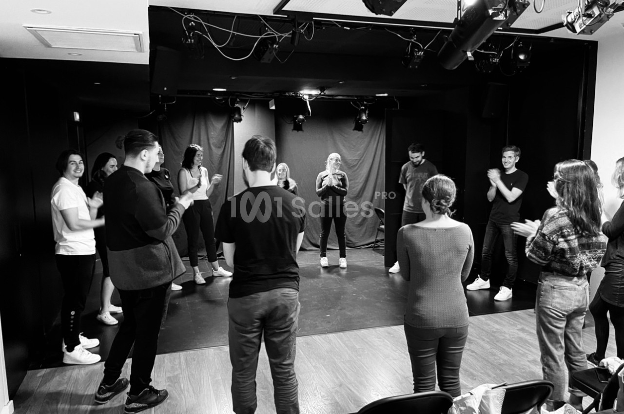 Un groupe de personnes en cercle dans une salle de théâtre, applaudissant et participant à une activité collective.