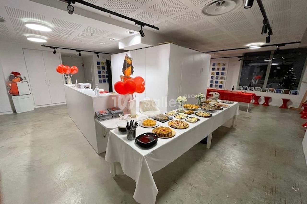 Buffet dressé dans une salle moderne avec nappes blanches, plats variés, ballons rouges et décoration minimaliste.