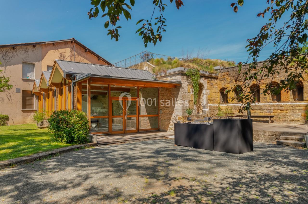 Bâtiment moderne avec façade vitrée à gauche et ruines en pierre à droite, entourés de verdure sous un ciel bleu.