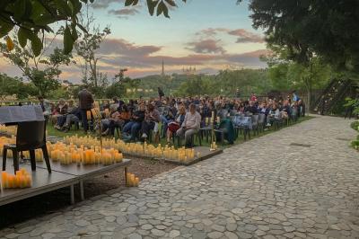 Vue nocturne d'un événement en plein air avec des stands sous une tente éclairée et des participants rassemblés.