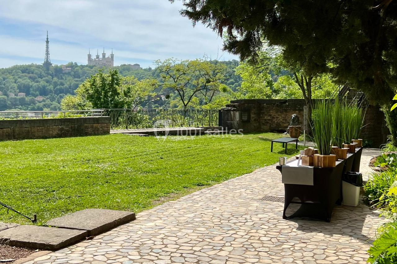 Allée pavée bordée de verdure avec vue sur une colline arborée et des monuments en arrière-plan.