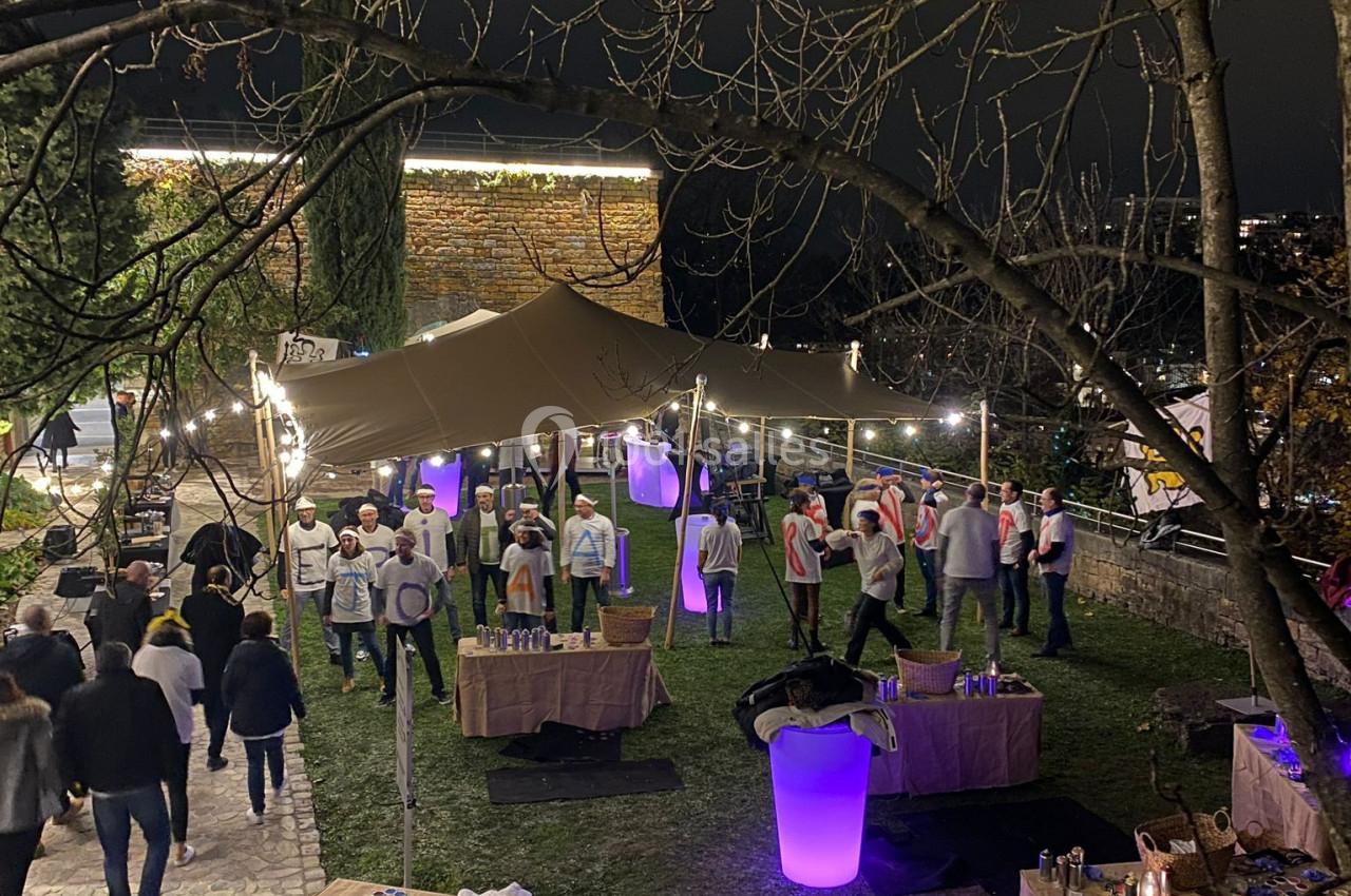 Vue nocturne d'un événement en plein air avec des stands sous une tente éclairée et des participants rassemblés.