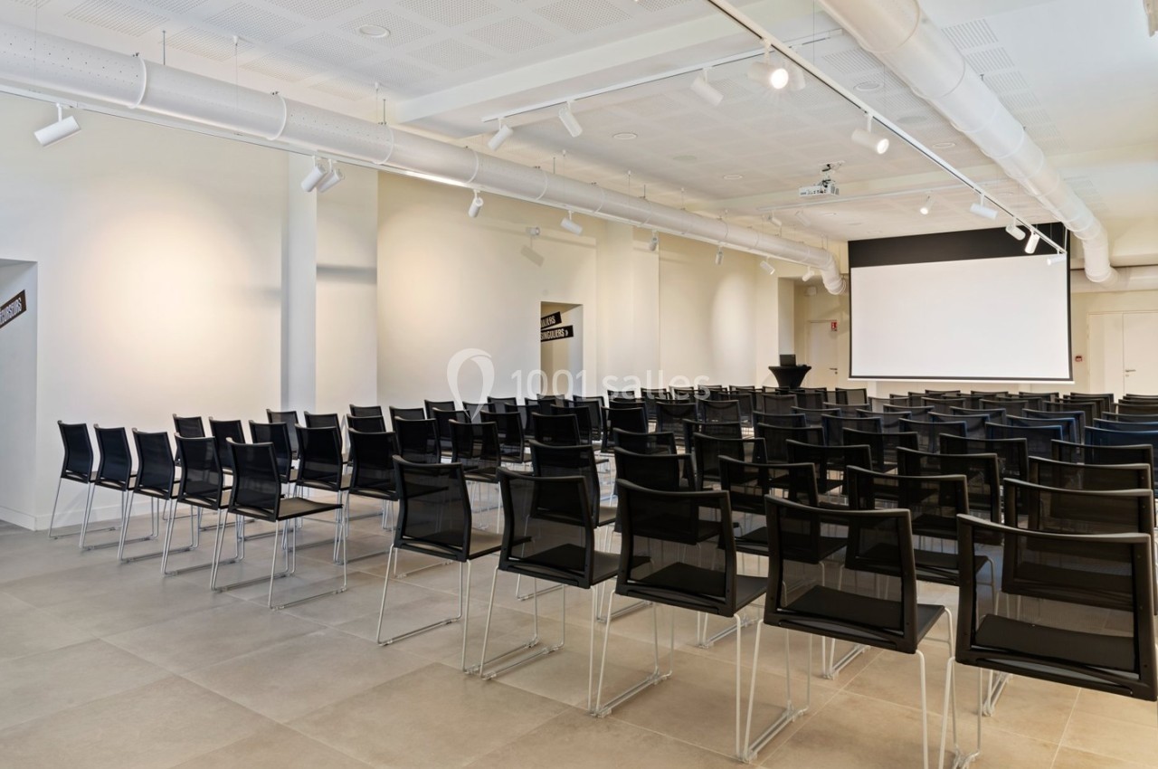 Location salle Lyon 9 (Rhône) - Le Fort de Vaise #2 Salle de conférence lumineuse avec des rangées de chaises noires et un écran de projection blanc à l'avant.