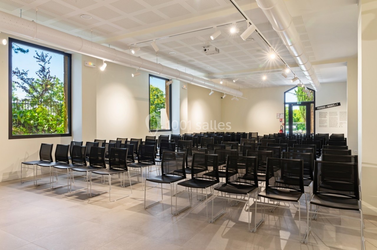 Location salle Lyon 9 (Rhône) - Le Fort de Vaise #3 Salle lumineuse avec des rangées de chaises noires alignées, grandes fenêtres donnant sur un espace verdoyant.