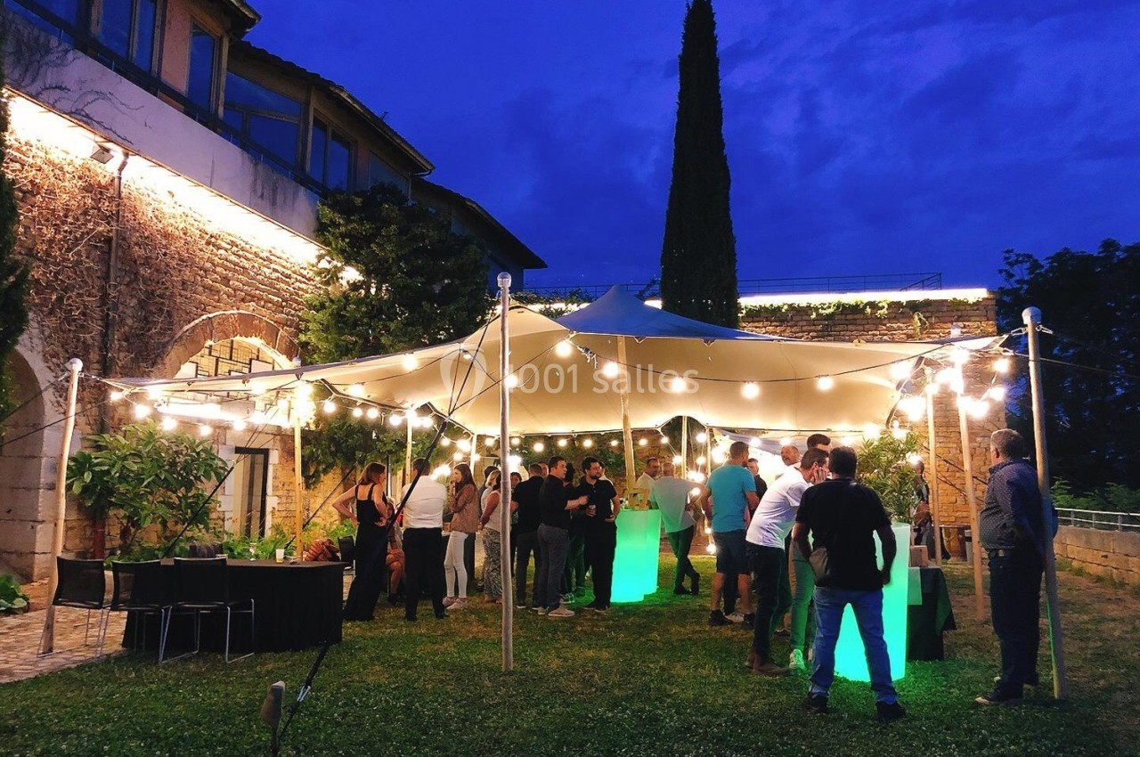 Location salle Lyon 9 (Rhône) - Le Fort de Vaise #4 Groupe de personnes rassemblées sous un chapiteau éclairé par des guirlandes lumineuses dans un jardin en soirée.