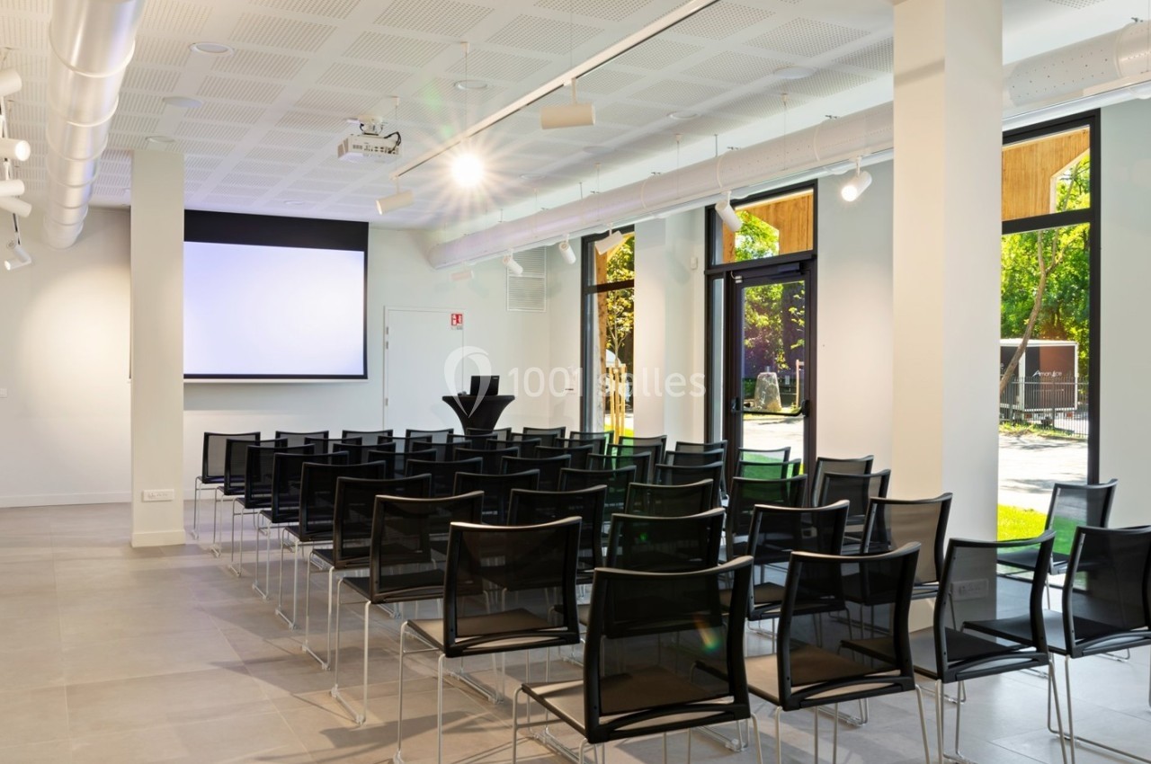 Location salle Lyon 9 (Rhône) - Le Fort de Vaise #8 Salle de conférence lumineuse avec des chaises noires alignées, un écran de projection et de grandes fenêtres donnant sur l…