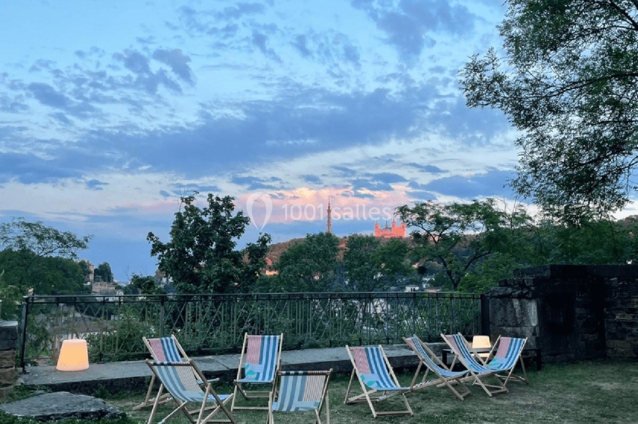 Location salle Lyon 9 (Rhône) - Le Fort de Vaise #13 Chaises longues colorées disposées sur une pelouse au crépuscule, avec vue sur des arbres et un ciel nuageux.