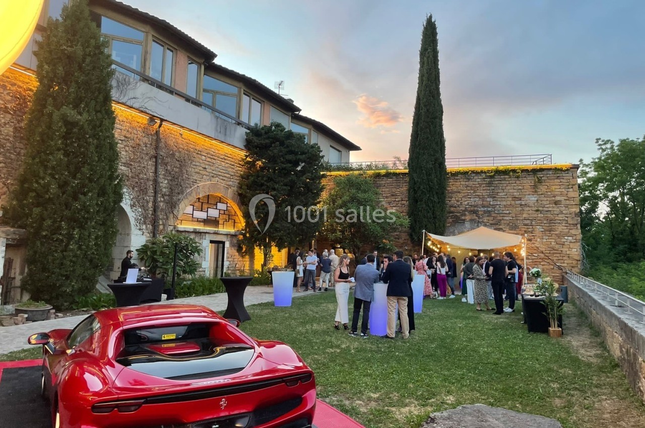 Location salle Lyon 9 (Rhône) - Le Fort de Vaise #18 Groupe de personnes rassemblées dans un jardin près d'un bâtiment en pierre, avec une voiture rouge au premier plan.