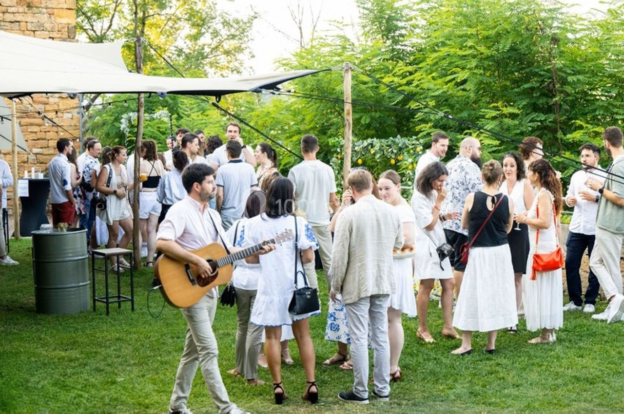 Location salle Lyon 9 (Rhône) - Le Fort de Vaise #19 Groupe de personnes en tenue estivale discutant et écoutant un musicien jouant de la guitare dans un jardin verdoyant.