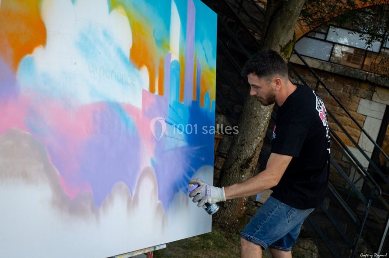 Location salle Lyon 9 (Rhône) - Le Fort de Vaise #22 Un homme peint une fresque colorée à la bombe sur une grande toile en extérieur.