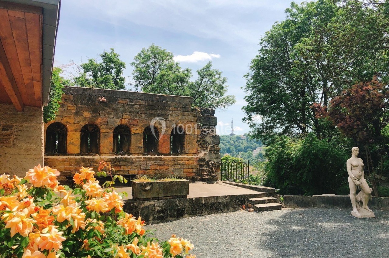 Location salle Lyon 9 (Rhône) - Le Fort de Vaise #23 Jardin avec statue, mur en pierre percé d'arches, fleurs orange au premier plan et arbres en arrière-plan.