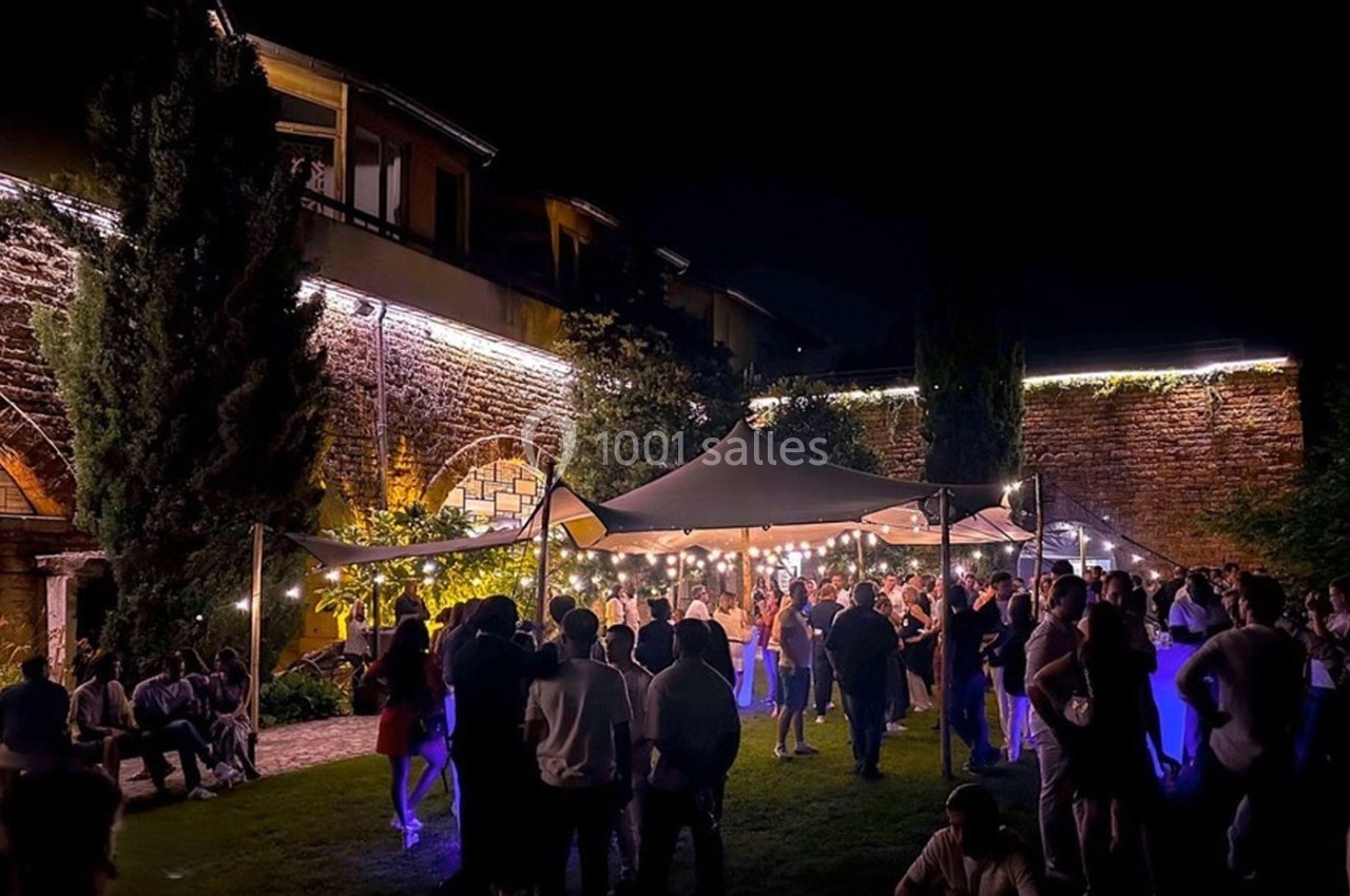Location salle Lyon 9 (Rhône) - Le Fort de Vaise #28 Groupe de personnes rassemblées sous un chapiteau éclairé dans un jardin, de nuit, avec des bâtiments en arrière-plan.