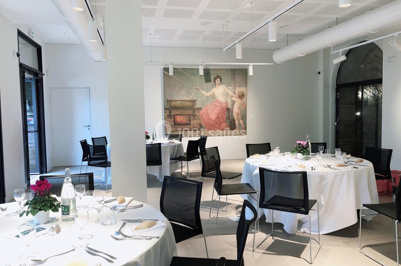 Location salle Lyon 9 (Rhône) - Le Fort de Vaise #31 Salle lumineuse avec tables rondes dressées pour un repas, décorée d'une grande peinture murale et de fleurs.
