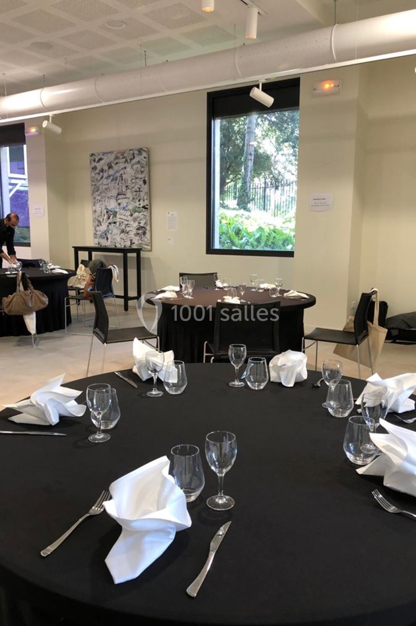 Location salle Lyon 9 (Rhône) - Le Fort de Vaise #39 Tables rondes dressées avec nappes noires, serviettes pliées et verres dans une salle lumineuse avec grandes fenêtres.