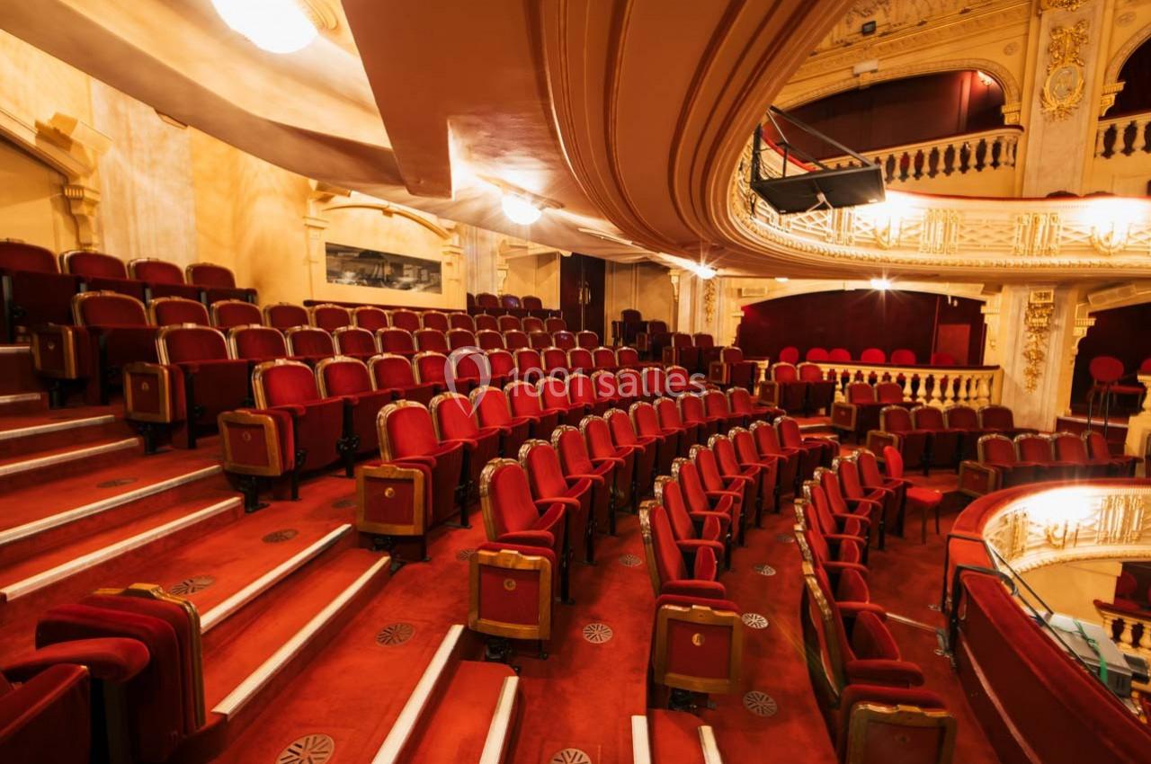 Salle de théâtre avec sièges rouges en velours, balcons ornés et éclairage chaleureux.