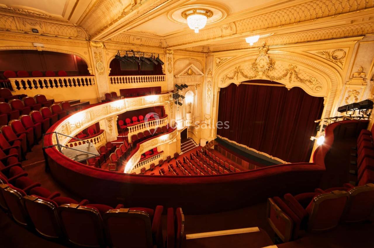 Salle de théâtre avec balcons ornés, sièges rouges et rideau de scène fermé dans un décor intérieur élégant.