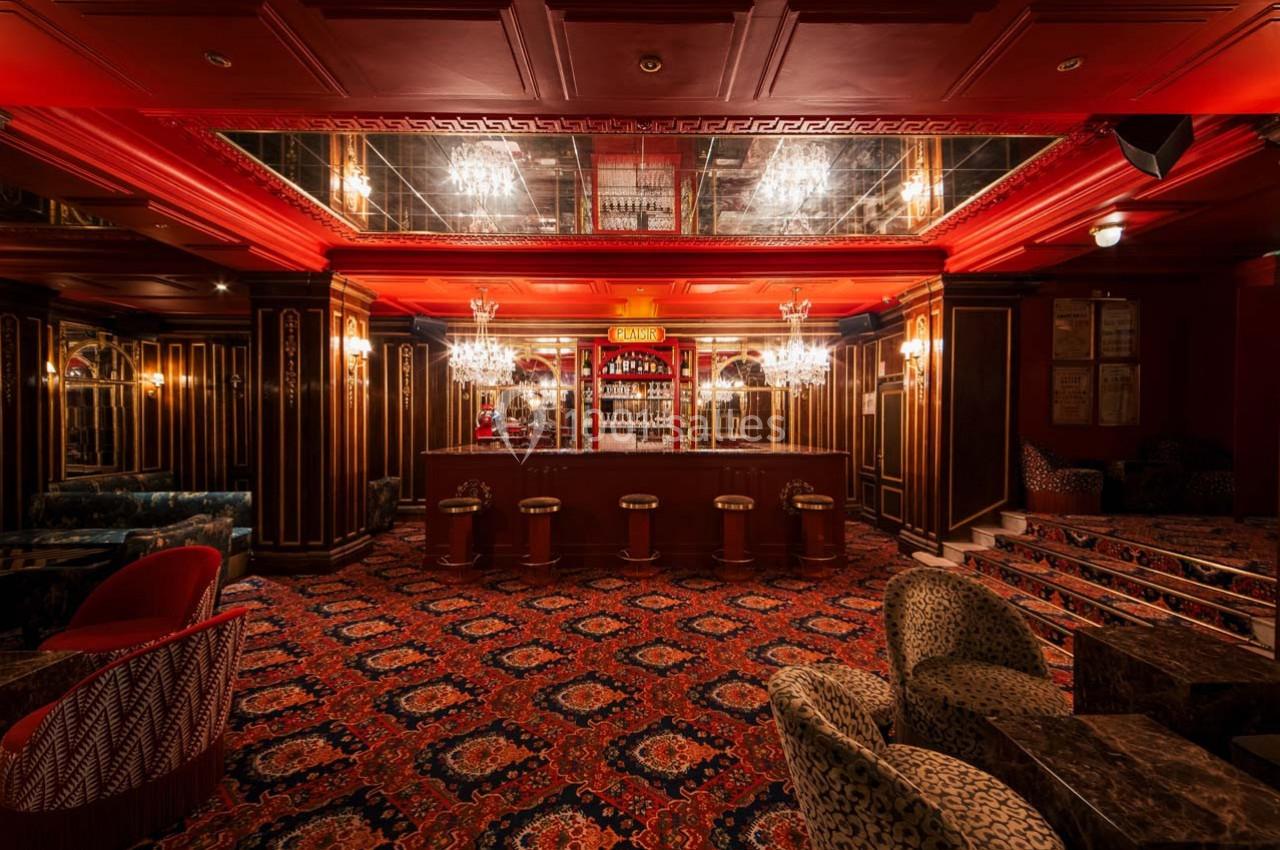Intérieur d'un bar élégant avec comptoir central, tabourets, moquette ornée et éclairage chaleureux.
