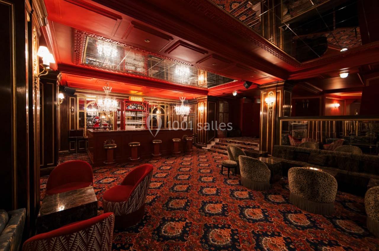 Salle de bar élégante avec moquette à motifs, fauteuils rembourrés, comptoir en bois et éclairage tamisé.