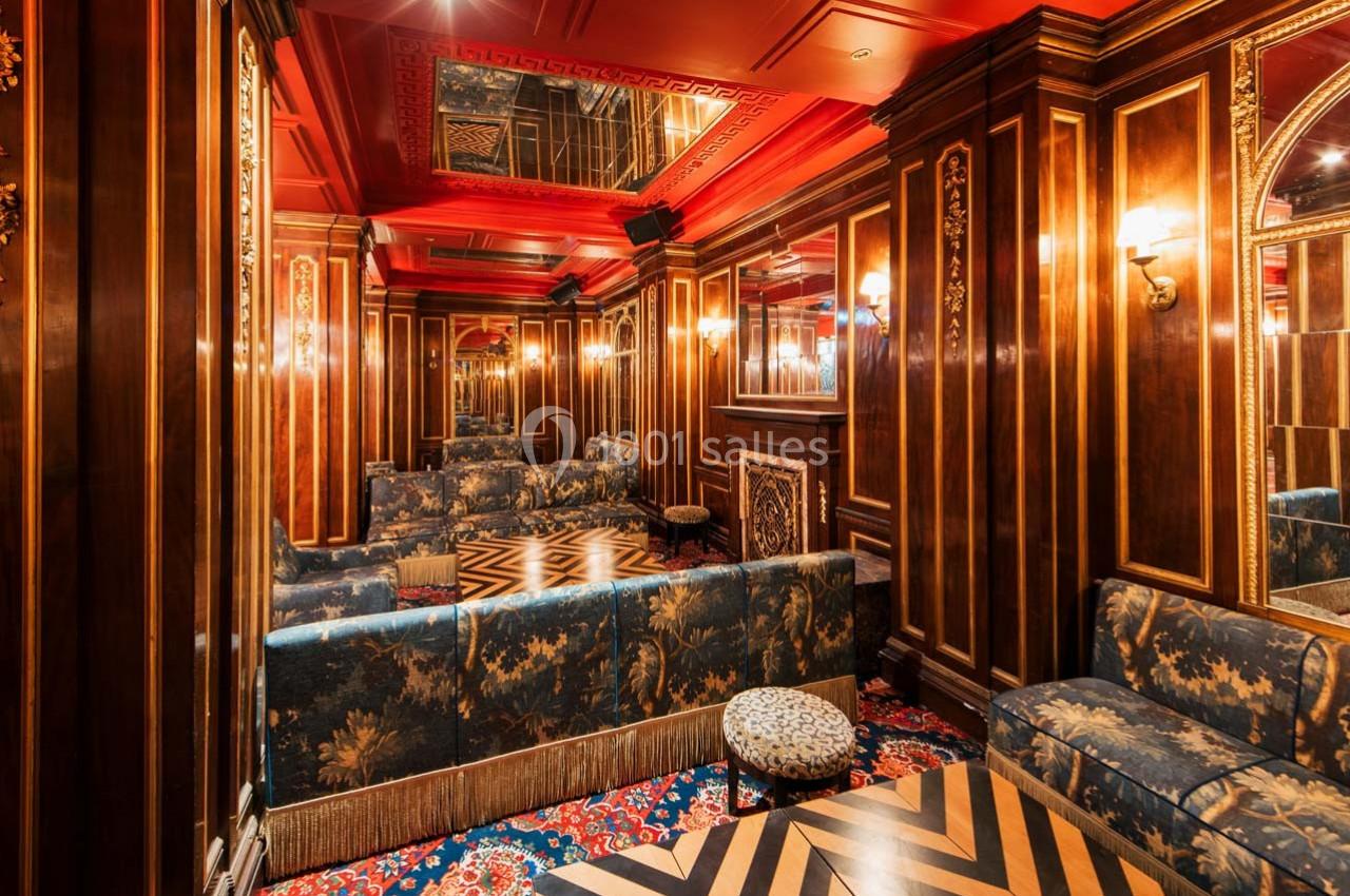 Salon élégant avec boiseries sombres, plafond rouge, miroirs, canapés fleuris et sol à motifs géométriques.