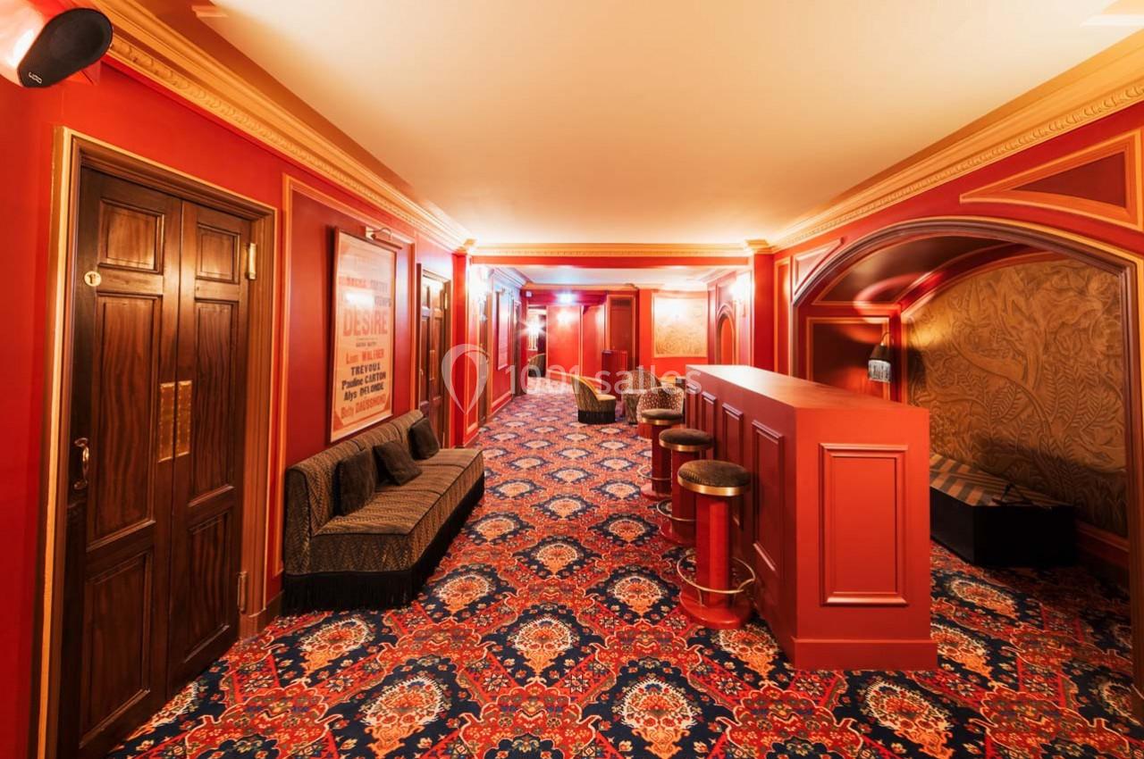 Couloir d'intérieur avec moquette colorée, murs rouges, banquettes, comptoir et éclairage tamisé.